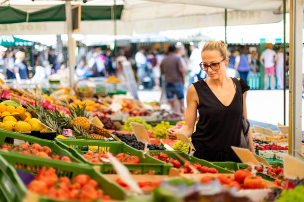 Kadın yerel gıda pazarından meyve ve sebze alıyor. Çeşitli organik sebzelerle market tezgahı - Fotoğraf, Görsel