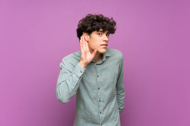 Young man over isolated purple wall listening to something by putting hand on the ear - Photo, Image
