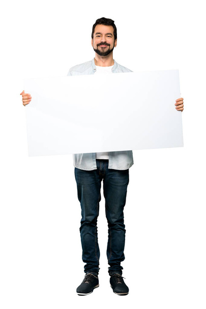 Full-length shot of Handsome man with beard holding an empty placard over isolated white background - Foto, afbeelding