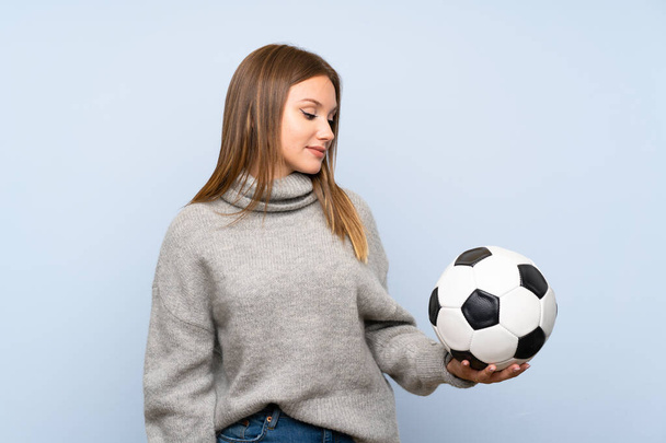 Девочка-подросток в свитере на изолированном синем фоне держит футбольный мяч
 - Фото, изображение