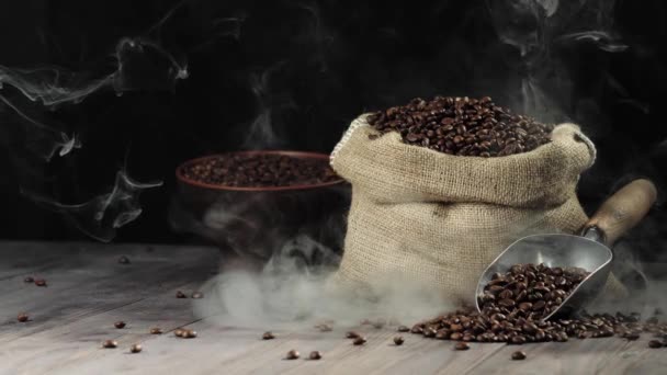 Composition from coffee beans. Wooden table background decorated with bag with coffee beans, bowl and scoop with fragrant coffee beans. Steam comes from the grains on the wooden table. Slow motion. 4K - Footage, Video