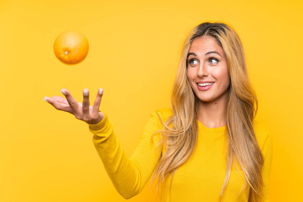 Genç sarışın kadın sarı arka plan üzerinde bir turuncu tutan - Fotoğraf, Görsel