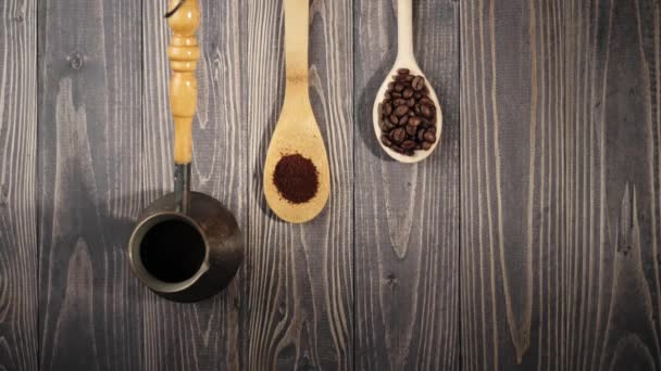 Koostumus kahvipavuista. Puinen pöytä tausta koristeltu kahvinkeitin ja puulusikat kahvia. Kahvipavut putoavat puupöytään. 4K
 - Materiaali, video