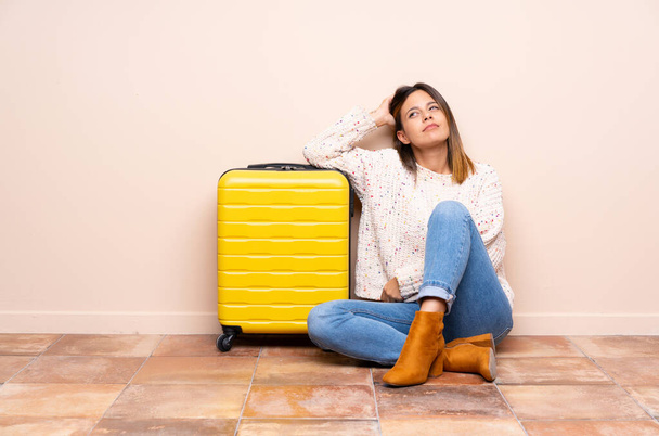 Traveler woman with suitcase sitting on the floor having doubts and with confuse face expression - Foto, Bild