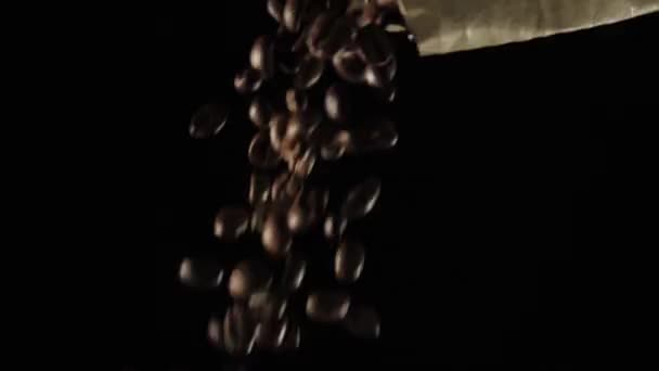Roasted coffee beans pour out of the pack down on black background. Fragrant fresh flying coffee beans. Close up. Slow Motion. - Footage, Video