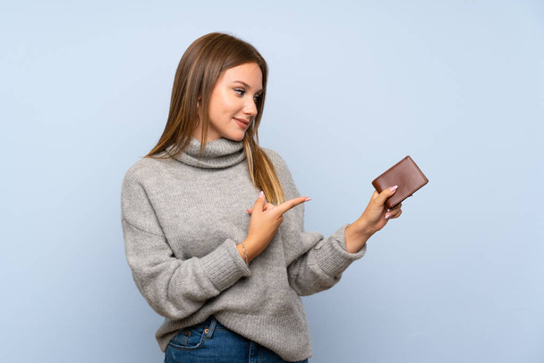 Tiener meisje met trui over geïsoleerde blauwe achtergrond houden van een portemonnee - Foto, afbeelding