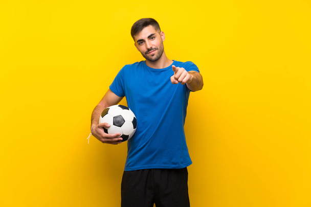 Giovane giocatore di calcio bello uomo oltre isolato muro giallo punta il dito contro di voi con un'espressione fiduciosa
 - Foto, immagini