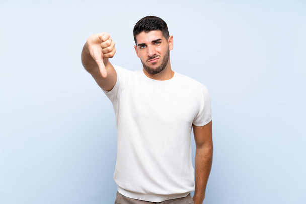 Caucasian handsome man over isolated blue background showing thumb down with negative expression - Photo, Image