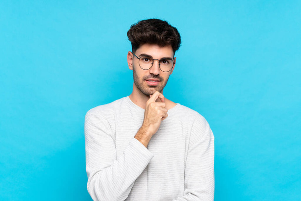 Young man over isolated blue background with glasses and smiling - Foto, afbeelding