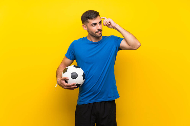 Jovem jogador de futebol bonito homem sobre parede amarela isolada com dúvidas e com expressão facial confusa
 - Foto, Imagem