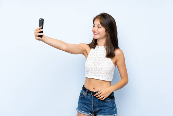 jonge vrouw over geïsoleerde blauwe achtergrond het maken van een selfie - Foto, afbeelding