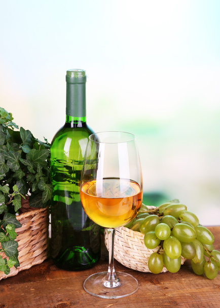 Ripe green and purple grapes in basket with wine on wooden table on bright background - Foto, imagen