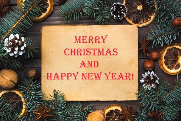 Marco de conos de árbol de Navidad naranjas nueces sobre fondo de madera oscura. Inscripción Feliz Navidad y feliz año nuevo
. - Foto, imagen