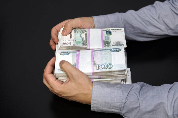 Mužské ruce popadly velkou sumu peněz. Anonymní obchodník natahuje ruku, aby sebral peníze, ruskou rublovou měnu, v temné místnosti - Fotografie, Obrázek