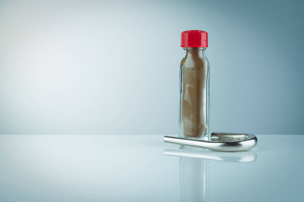 Ταϊλανδικό φυτικές σκόνες ταμπάκο σε διαφανές γυάλινο μπουκάλι με κόκκινο καπάκι και ταμπάκο σωλήνα. Καφέ σκόνες με κενή ετικέτα σε φιάλη που απομονώνεται σε βαθμωτό φόντο. Ταϊλανδέζικη παραδοσιακή ιατρική Φαρμακευτική. - Φωτογραφία, εικόνα