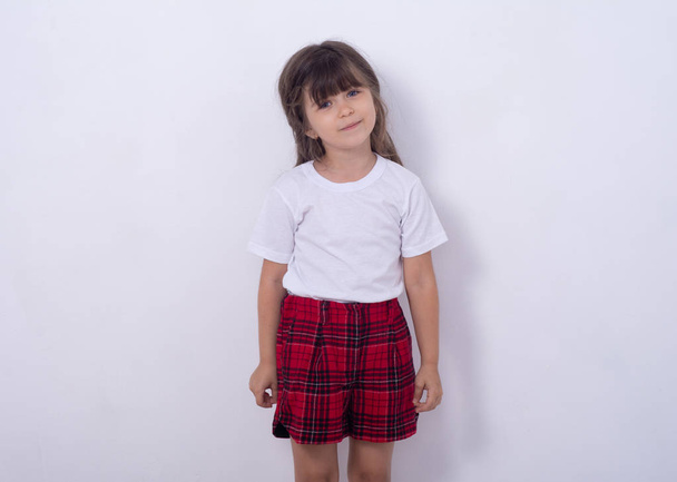 Child 5 or 6 years old with curly hair and a white t-shirt posing on a white background. Happy expression. Isolated ad - 写真・画像