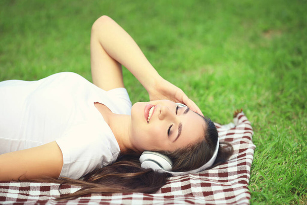 Young happy girl lying on green grass and listening music with h - Foto, imagen