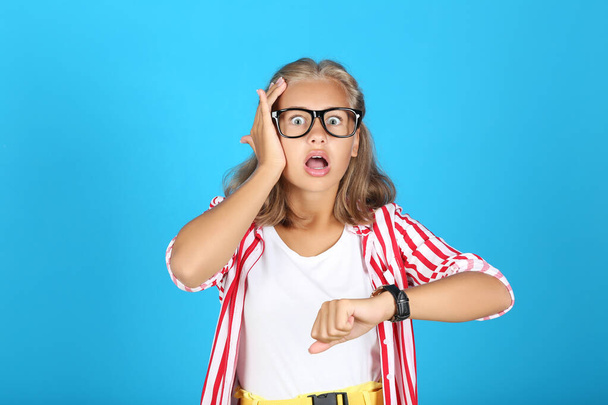 Young surprised girl with wrist watch on blue background - Foto, imagen