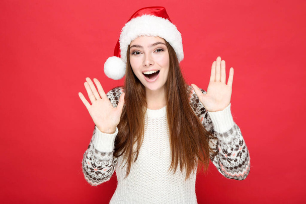 Beautiful woman in sweater and santa hat on red background - Foto, afbeelding