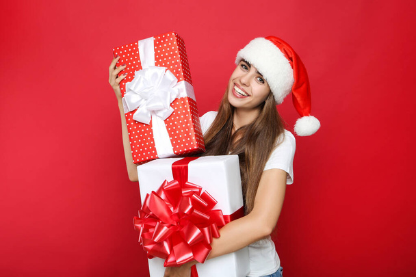 Beautiful woman wearing santa hat and holding gift boxes on red  - Fotografie, Obrázek