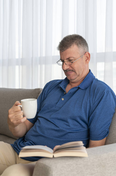 middle aged man on his sofa reading a book - Foto, Imagen