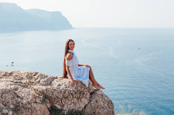 mooie vrouw met lang haar in jurk op klif klif door de zee - Foto, afbeelding