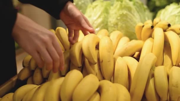 Mujer eligiendo plátanos en tienda de comestibles. Chica tomar plátano en el supermercado. Concepto de compras
 - Imágenes, Vídeo