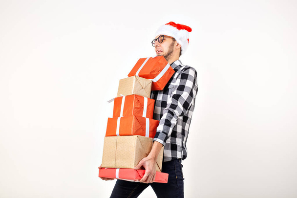 Διακοπές και παρουσιάζει έννοια - Αστείος άνθρωπος στο καπέλο Χριστούγεννα κρατώντας πολλά κουτιά δώρων σε λευκό φόντο με αντίγραφο χώρο - Φωτογραφία, εικόνα