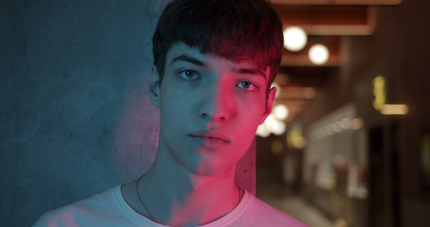 Portrait of Young Millenial Stylish Guy Turning Head and Looking Straight to Camera Standing at Futuristic Neon Club Lights. Lifestyle and People Concept. Close Up. - Materiał filmowy, wideo