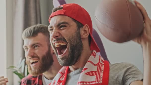 Два весёлых бородатых фаната мужчины радуются и кричат, наблюдая за спортом в квартире
 - Кадры, видео