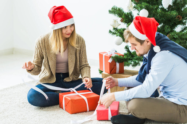 Holidays concept - Sweet couple opening Christmas gifts, sitting in the living room - Photo, Image