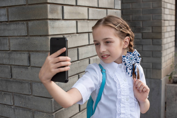 Mosolygó, gyönyörű, fiatal lány, aki szelfit csinál a szabadban. A gyerek önarcképet készít mobiltelefonnal. technológia - Fotó, kép
