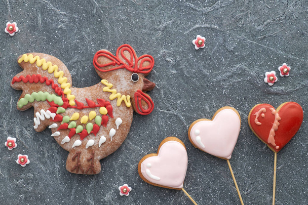 Gingerbreads shaped as a rooster bird and hearts on dark textured background - Photo, image