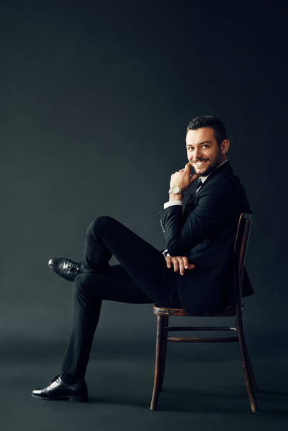 Happy successful man in black suit smiling and looking to camera sitting on chair - 写真・画像