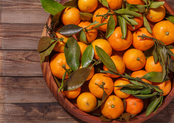 Mandarin oranges with leaves in wooden plate on rustic wood background. Winter fruits. - Foto, Imagem