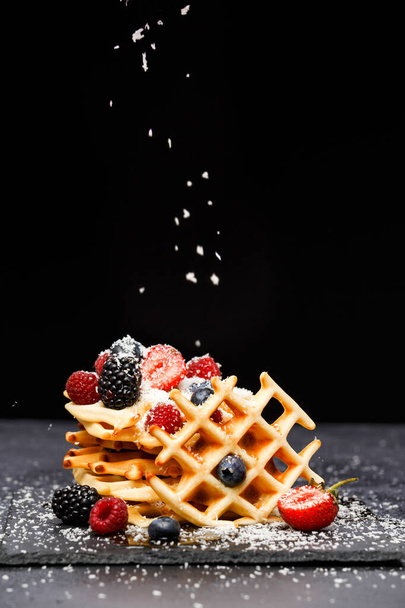 Foto di waffle viennesi freschi con bacche cosparse di zucchero a velo su lavagna su sfondo bianco in studio
 - Foto, immagini