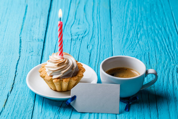 Kremalı ve yanan mumlu çörekler kahve fincanının yanında ve mavi masada boş bir kart. - Fotoğraf, Görsel