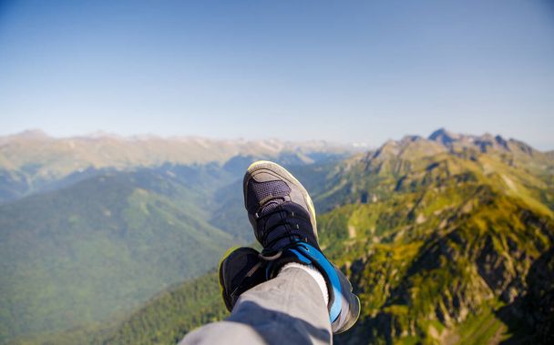 Photo of man in sneakers and picturesque mountainous landscape against blue sky - 写真・画像