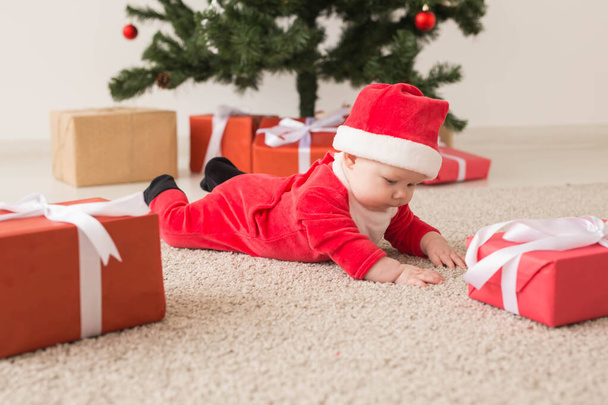 Schattig meisje in kerstpak kruipend op de grond boven de kerstboom. Vakantie seizoen. - Foto, afbeelding