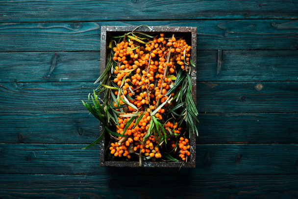 Twigs with sea buckthorn berries on a blue wooden background. Top view. Free space for your text. - Foto, Imagen