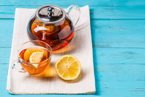 Glas Tee mit Zitrone und Glas Teekanne auf blauem Holztisch. - Foto, Bild