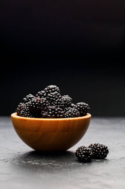Photo of blackberry in wooden cup on empty black background in studio - Fotó, kép