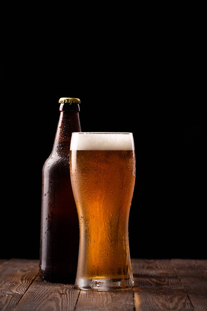 Fénykép Buttle és üveg sör asztalnál és fekete háttér mögött - Fotó, kép