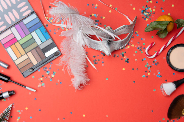 Picture on top of eye shadows, brushes, feather mask, tangerine, sugar cane,confetti on empty red table, place for inscription - Photo, Image