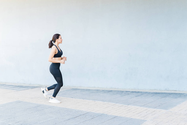 Beyaz kadın sporcunun yürüyüş yolunda duvarda koşuşunun yan görüntüsü - Fotoğraf, Görsel