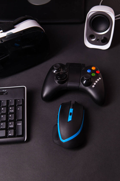 Vista superior de un equipo de juego, ratón, teclado, joystick, auriculares, VR auriculares sobre fondo de mesa negro. Concepto de espacio de trabajo Gamer
. - Foto, imagen