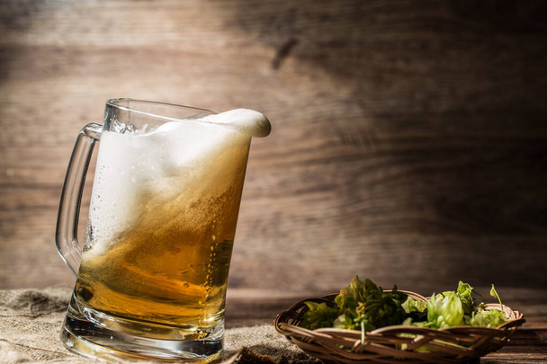 Βρώμικη μπύρα χύνεται από κούπα στέκεται σε λινό ύφασμα σε άδειο ξύλινο φόντο - Φωτογραφία, εικόνα