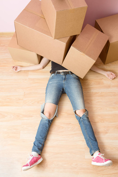 Imagen de la mujer en jeans acostada debajo de cajas de cartón en nuevo apartamento
 - Foto, imagen