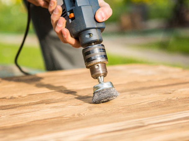 Mãos homem com disco de metal escova rotativa elétrica lixando um pedaço de madeira. Trabalhos em madeira ao ar livre
. - Foto, Imagem