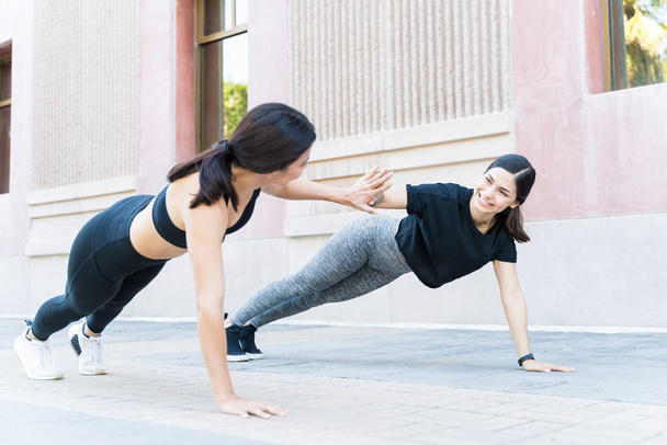 Smiling fit women giving high-five while doing push-ups on footpath - Photo, Image